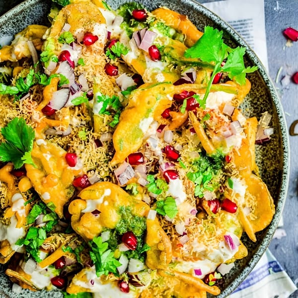 Colorful Indian chaat with fried fritters, yogurt, chutneys, pomegranate, onions, and cilantro in a bowl.