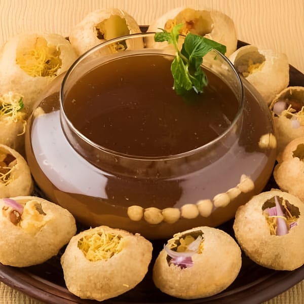 Crispy Pani Puri shells filled with savory ingredients, surrounding a bowl of mint-garnished tamarind water.
