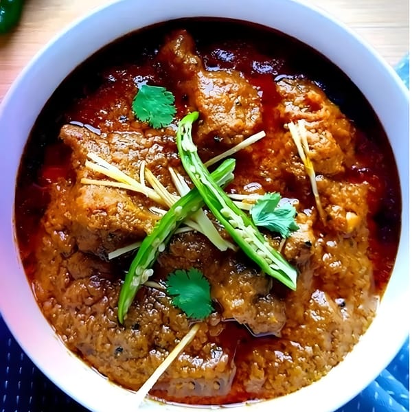 Rich, spicy curry with meat, garnished with green chilies, ginger, and cilantro.