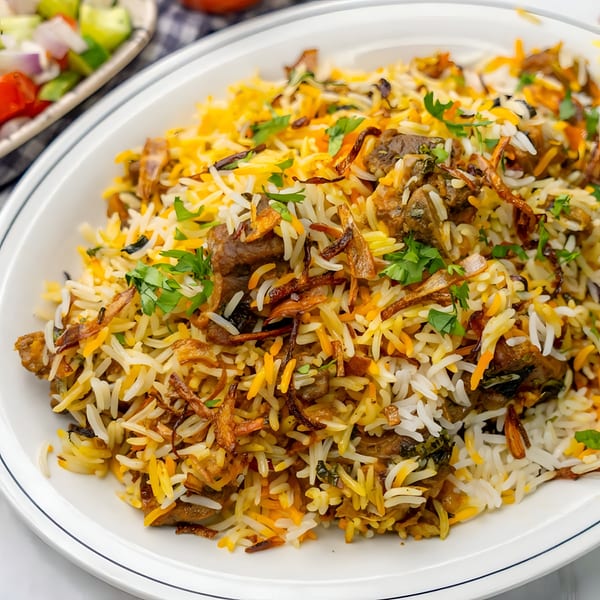 Close-up of a large plate of biryani with meat, rice, fried onions, and cilantro.